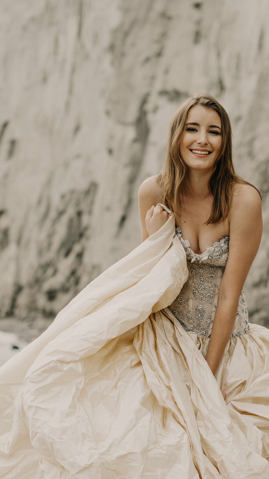 Woman in a flowing dress standing on a beach with cliffs in the background